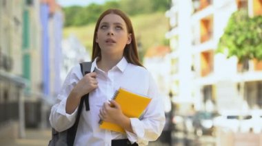 Sırt çantası ve kitapları olan hoşnutsuz bir kız öğrenci kameraya ve eğitime bakıyor.