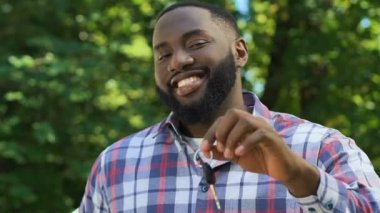 Duygusal Afro-Amerikalı adam kameranın otomatik anahtarını gösteriyor, kredi alıyor.