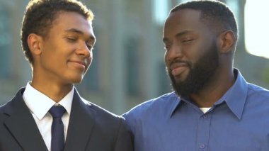 Afro-Amerikalı baba ve oğlu resmi giyinmiş kameraya bakıyor ve gülümsüyor, aile