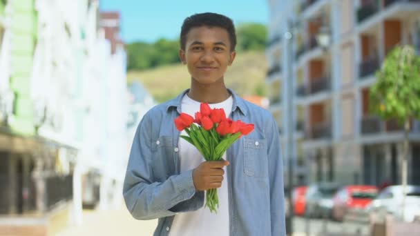 Happy afro-american young male holding tulips bouquet and smiling on camera gift — Stock Video