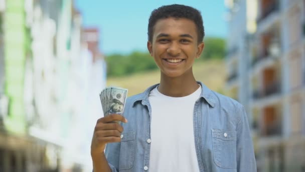 Cheerful black teen guy holding dollars bunch and smiling on camera first income — Stock Video