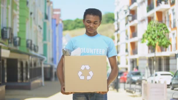 Gelukkig gemengd ras tiener mannelijke eco-vrijwilliger holding papieren doos met recycling teken — Stockvideo