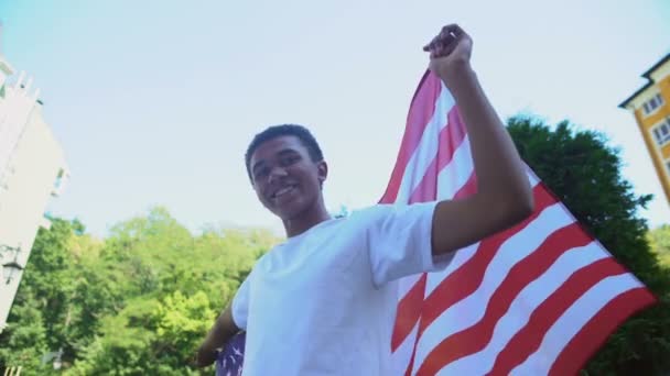 Emocionado adolescente birracial ondeando bandera nacional de EE.UU. y sonriendo, día de la independencia — Vídeo de stock