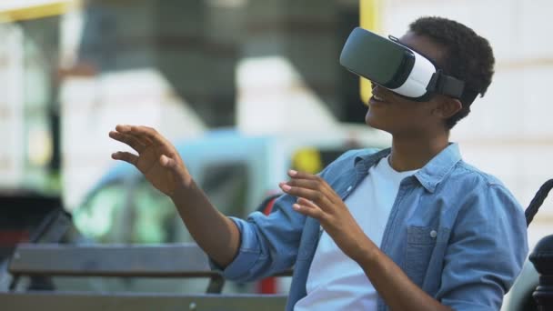 Teenie-Junge mit gemischter Rasse sitzt in Virtual-Reality-Headset auf Bank, modernes Gerät — Stockvideo