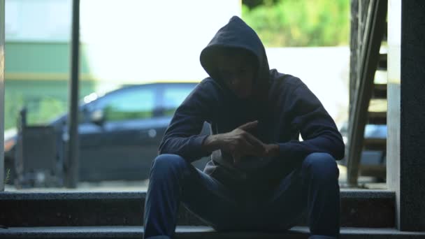 Депрессивный черный мальчик, сидящий на лестнице и размышляющий о тяжелой жизни в гетто — стоковое видео