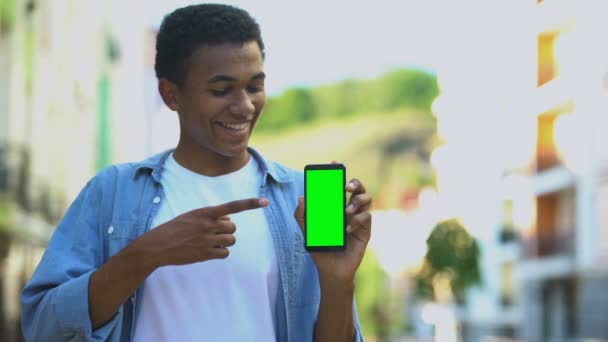 Улыбающийся подросток держит смартфон с зеленым экраном, навигационное приложение — стоковое видео