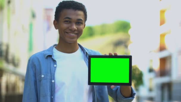 Возбужденный черный мальчик показывает пальцем на зеленый экран планшета в руке, реклама — стоковое видео