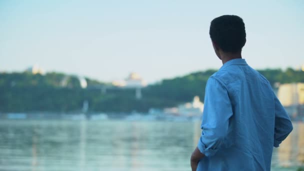 Afrikanisch-amerikanischer Kerl ruht sich auf dem Flussufer aus und genießt den Blick auf die Stadt, die Landschaft — Stockvideo