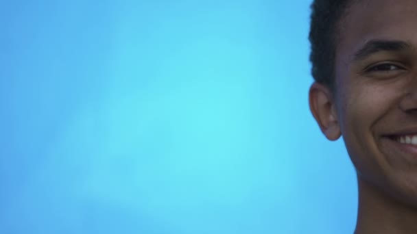 Half-face detailní záběr smíšené rasy teenager na modrém pozadí, studentské statistiky — Stock video