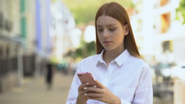 Молодая рыжая женщина, прокручивающая социальную сеть на смартфоне, шокирована новостями — стоковое видео