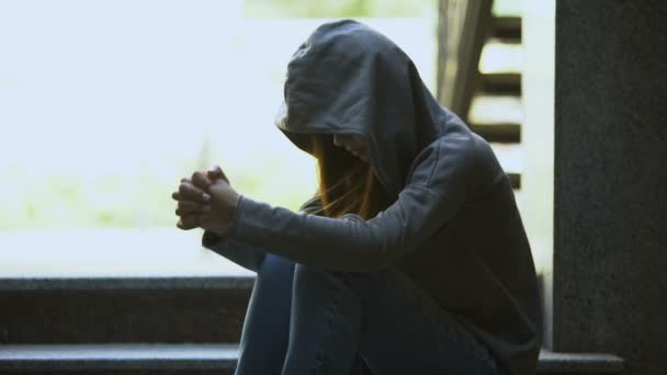 Depressive junge Frau im Kapuzenpulli sitzt allein auf der Treppe und denkt über Probleme nach — Stockvideo