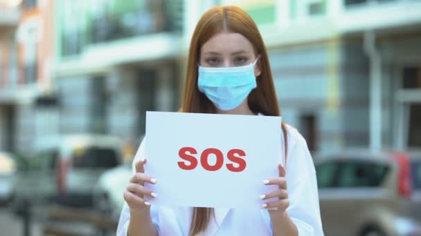 Молодая женщина в защитной маске держит знак SOS, загрязнение воздуха, парниковых газов — стоковое видео