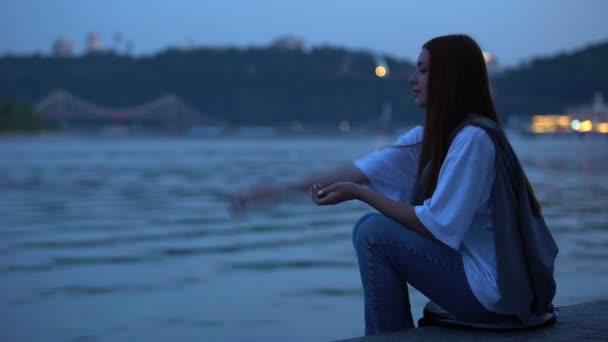 Zamyšlený dospívající dívka sedí na břehu řeky těší klidný letní večer — Stock video