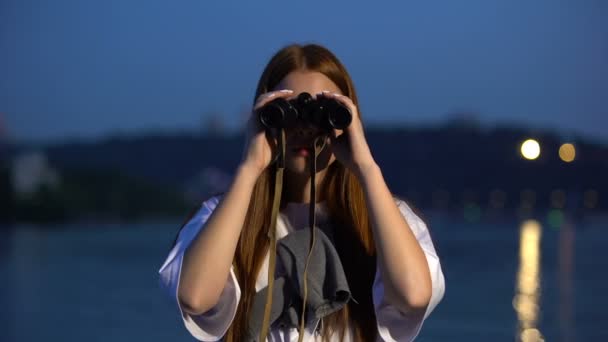 Chica curiosa pasando la noche en el terraplén del río, mirando a través de los prismáticos — Vídeos de Stock