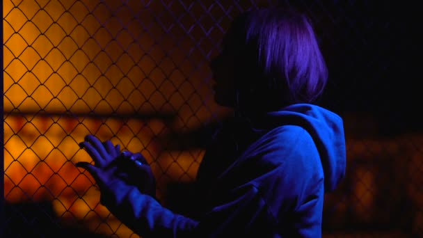 Грустная девочка-подросток прячется возле проволочного забора, семейный кризис, неловкий возраст — стоковое видео