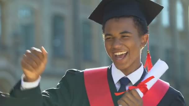 Vicces afro-amerikai fiú köntösben, diplomával és táncmozdulatokkal. — Stock videók
