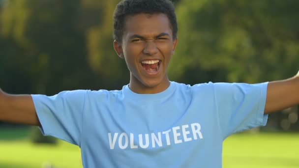 Lindo adolescente voluntario haciendo fuerte gesto y sonriendo a la cámara, caridad — Vídeos de Stock