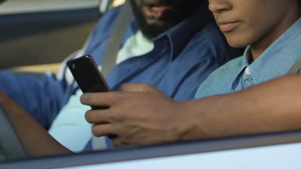 Afro-americano homem infeliz com adolescente rolando smartphone no assento do motorista — Vídeo de Stock