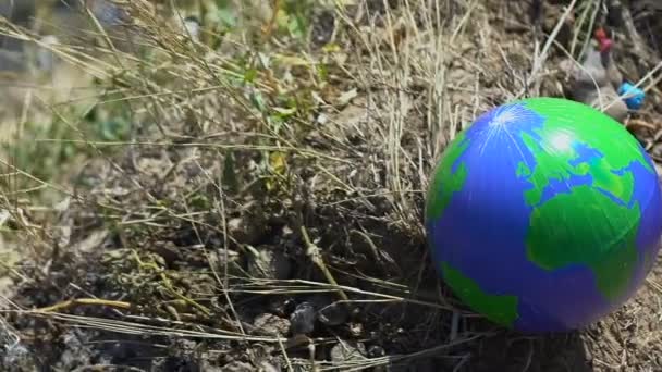 Глобусный шар, лежащий на траве возле свалки, экологическая опасность, опасность — стоковое видео