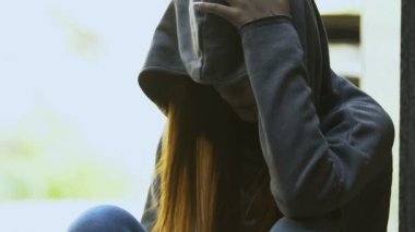 Yalnız, kızıl saçlı, kapüşonlu kadın şişeden bira içiyor. Umutsuzluk sorunu.