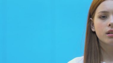 Mavi arka planda, ergenlik çağında, kendine güveni olmayan üzgün bir genç kız.