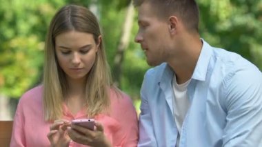 Genç adam uzlaşmaya çalışıyor ve kız arkadaşına sarılıyor. Telefonu kullanıyor, onu görmezden geliyor.