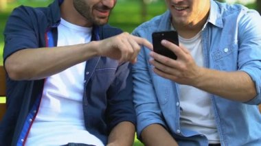 İki arkadaş akıllı telefondan komik videolar izliyor parkta bankta oturuyor, yakın plan çekimde.