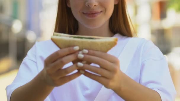 Улыбающаяся молодая женщина показывает сэндвич-камеру, органические закуски, вегетарианское питание — стоковое видео
