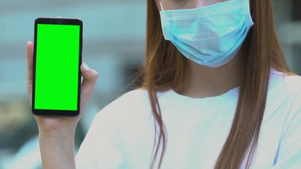 Sjuk kvinna i skyddsmask visar grön skärm smartphone, sjukhus app — Stockvideo