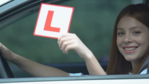 Gülümseyen genç bir bayan, L plakalı oturma arabasını gösteriyor, ehliyet sınavı var. — Stok video