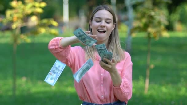 Joven ganadora de la lotería lanzando dólares y sonriendo en cámara, fortuna — Vídeo de stock