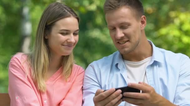 Jeune homme montrant femelle dans l'amour jeu vidéo sur téléphone portable dans le parc, sympathie — Video