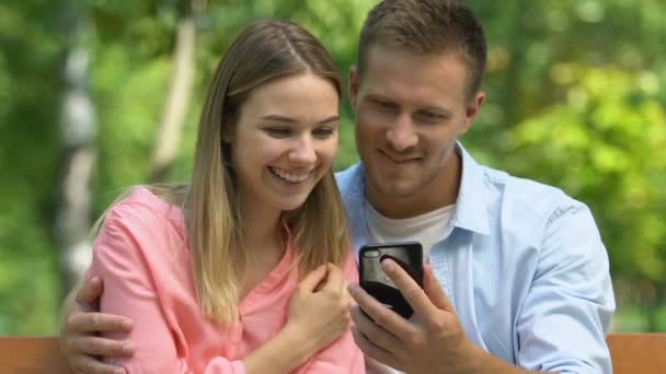 Joyeux couple amoureux regardant une vidéo drôle sur smartphone, rendez-vous romantique au parc — Video