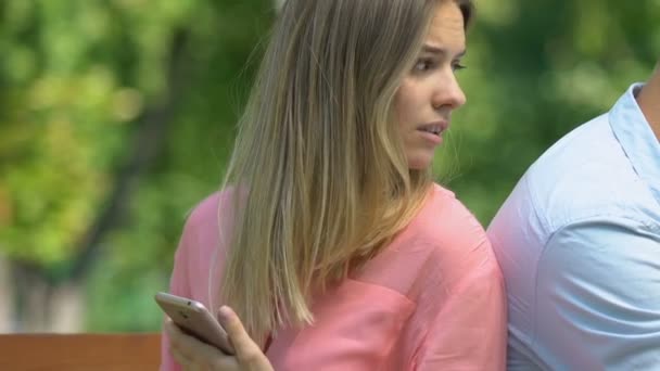 Ревнивая женщина с телефоном, наблюдающая за тем, как бойфренд болтает по телефону, недоверие — стоковое видео