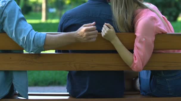 Женщина обнимает одного мужчину, держа за руку другого, сидит на скамейке, предает — стоковое видео