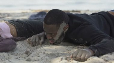 Bilinci olmayan bir kızın yanında acı çeken siyah bir adam, gemi enkazı kurbanı.