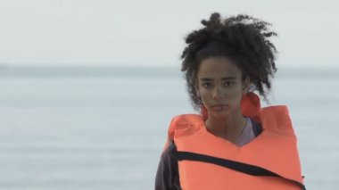 Can yeleği giymiş yaralı Afro-Amerikalı bir kız kameraya bakıyor, uçak kazası kurbanı.