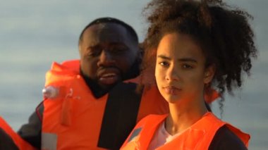 Can yelekli kızı olan Afro-Amerikalı bir adam kameraya, uçak kazasına bakıyor.