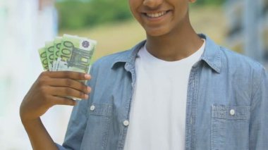 Mutlu genç çocuk bir tomar para gösteriyor, üniversite için tasarruf, depozito