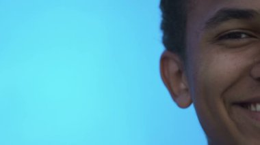Mavi arka planda kameraya gülümseyen neşeli siyahi çocuk.