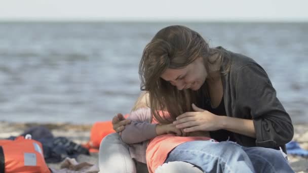 Gråtande kvinna håller medvetslös dotter på havskusten, skeppsbrutna offer — Stockvideo