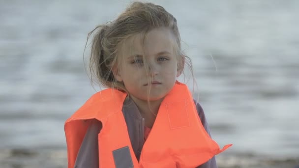 Одинокая девушка в спасательном жилете смотрит в камеру, поведение в чрезвычайных ситуациях — стоковое видео