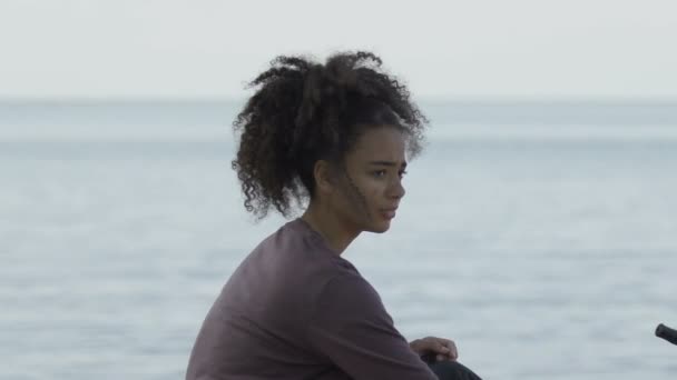 Sad Afro-American girl sitting near lifeboat on sea coast, shipwreck victim — Stock Video