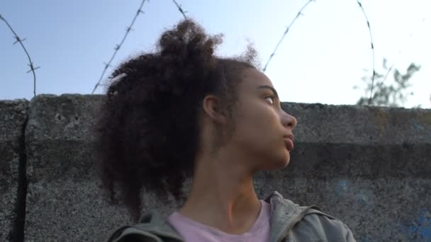 Афроамериканский подросток-беженец смотрит на стену с колючей проволокой перед побегом — стоковое видео