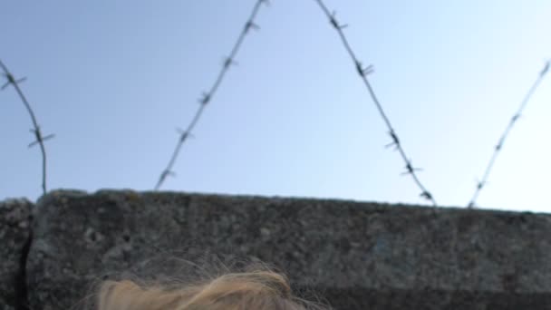 Meisje kijkt naar muur met prikkeldraad, droomt over vrijheid, vluchteling — Stockvideo
