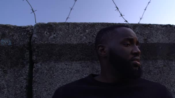 Douloureux visage de fermeture afro-américain masculin avec les mains derrière le mur de fil de barbier — Video