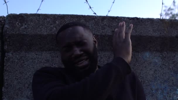 Płaczący czarny uchodźca stojący za ścianą drutem fryzjerskim, więzienie polityczne — Wideo stockowe