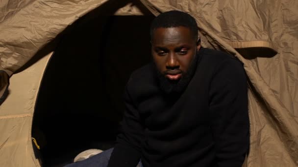 Deprimido afro-americano masculino vivendo na tenda olhando para a câmera, pobreza — Vídeo de Stock