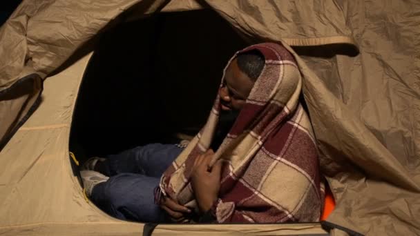 Ağlayan Afro-Amerikalı evsiz adam battaniyeyle örtülmüş çadırda yaşıyor, fakirlik içinde. — Stok video