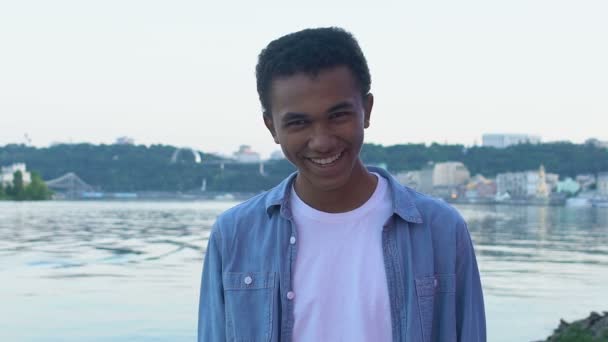Czarny nastolatek chłopiec śmieje się szczerze stojąc przed miejskim krajobrazem, ciesząc się życie — Wideo stockowe
